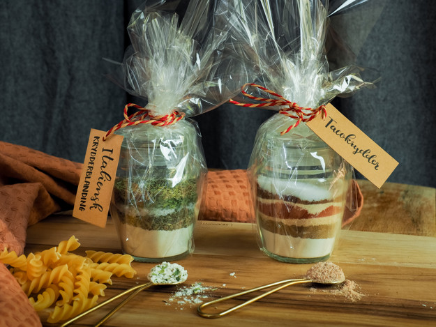 to glasskrukker med innhold i ulik farge som ligger lagvis. cellofan utenpå og lapp med navnene på krydderne. 