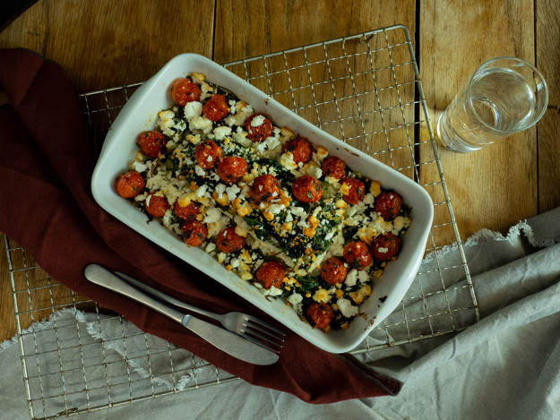 Torsk med tomat, spinat og fetablanding i en ildfastform. Ligger på en risk med bestikk, glass og rød serviett